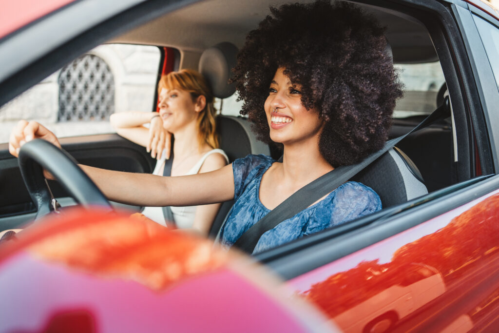 Two young female students driving a red car, which is a safer car colour according to research