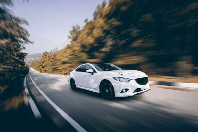 White car driving on tar road in the daytime