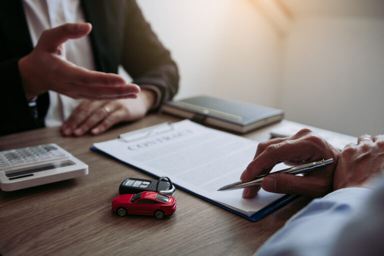 Car sales agreement on a desk, where 2 people sit and consider whether to get an Extended or Normal Vehicle Warranty.