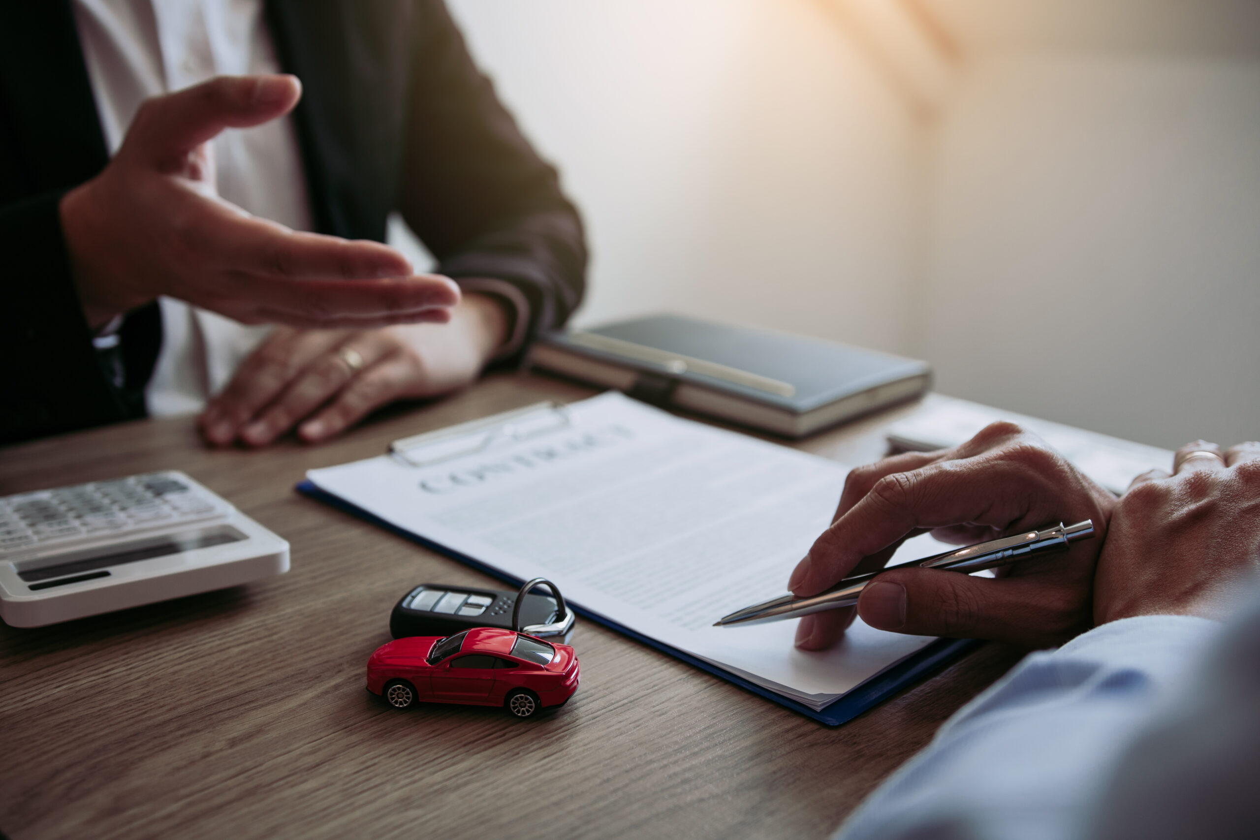 Car sales agreement on a desk, where 2 people sit and consider whether to get an Extended or Normal Vehicle Warranty.