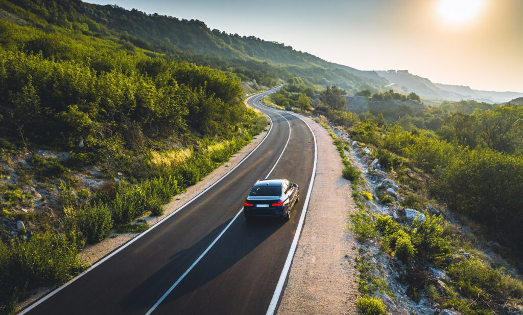 A black vehicle driving down a scenic road, showing that black is a car colour that is difficult to see.