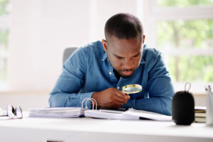 Black man reading a Vehicle warranty contract with a magnifying class to ensure he does not miss the fine print.